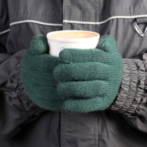 Person holding coffee in winter coat and green gloves