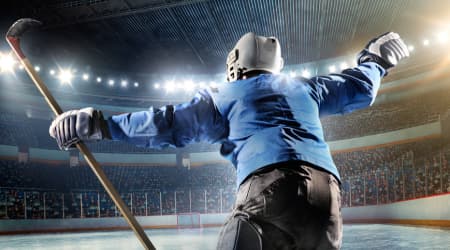 Young boy celebrating Ice Hockey goal holding Ice Hockey Stick, wearing blue Jersey