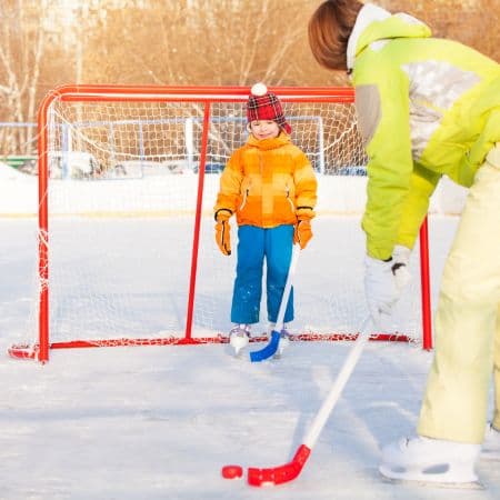 Mom teaching young child in front of a gaol teaching the game of Ice Hockey