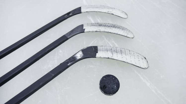 Three black hockey sticks wrapped in white tape with hockey puck on ice